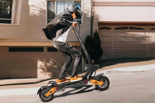 Dynamic suburban residential action shot of a helmeted rider cruising black-and-orange Freeboy H9 electric scooter along a neighborhood street in front of a family home.