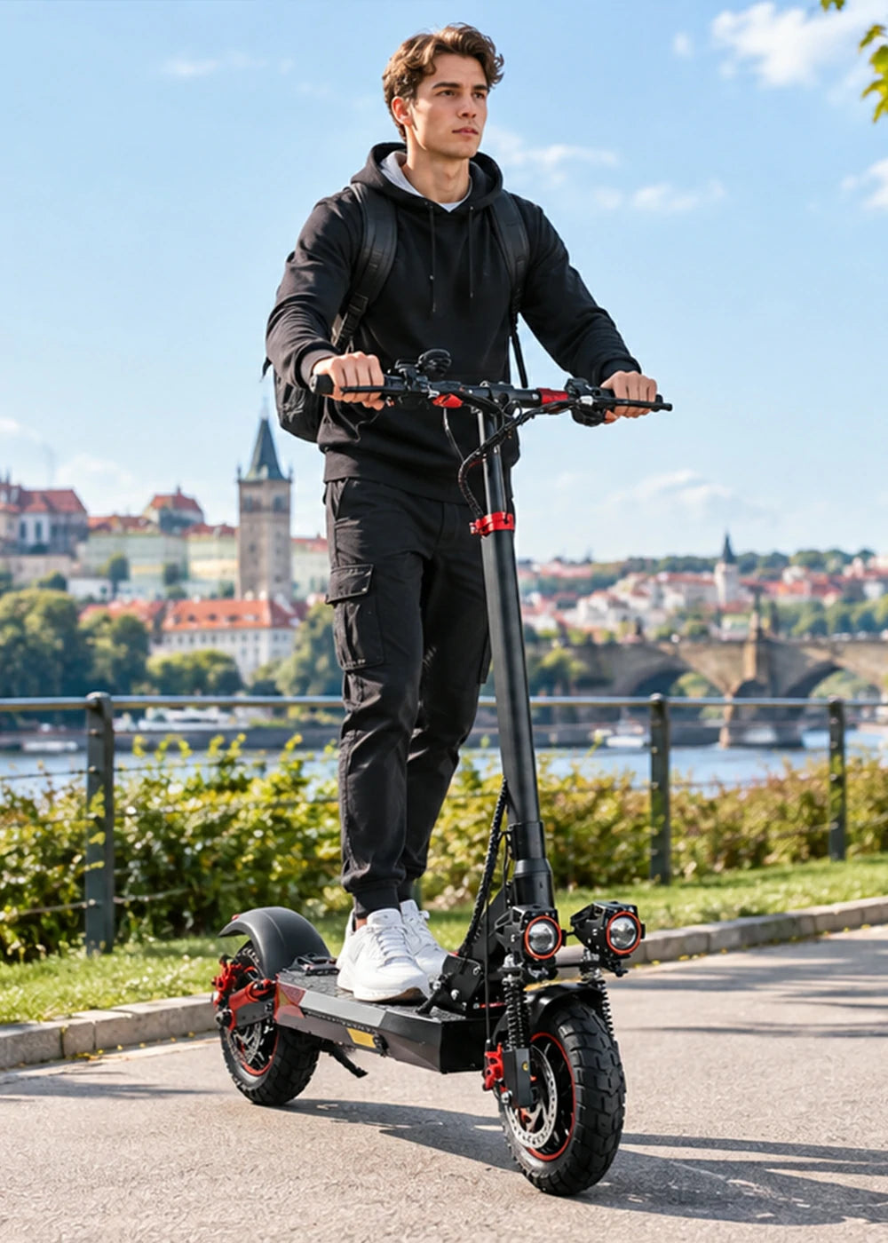 Young man riding Freeboy J01 electric scooter along Prague riverside promenade.