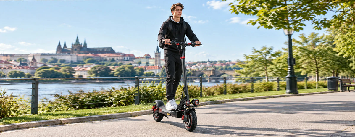 Young man riding Freeboy J01 electric scooter along Prague riverside promenade.